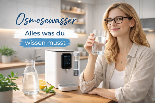 Frau in moderner Küche trinkt ein Glas Osmosewasser neben einer Auftisch-Osmoseanlage auf Holzarbeitsplatte